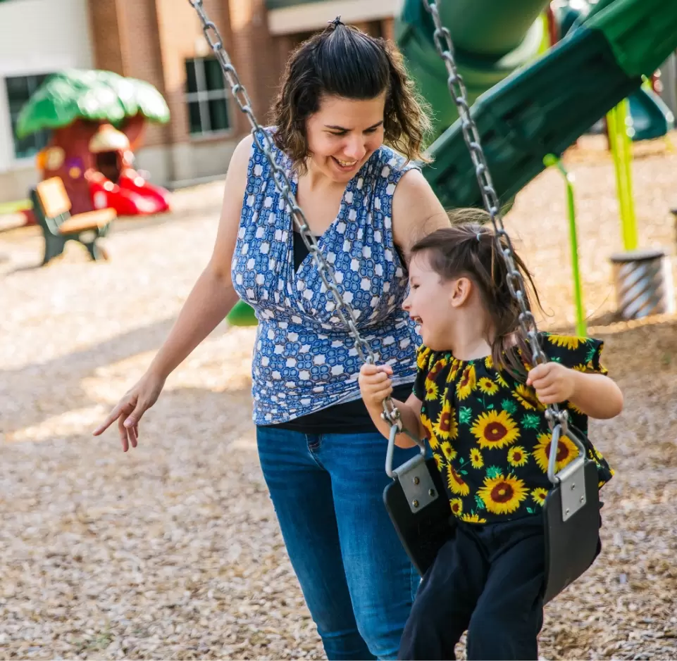 woman pushing a girl on a swingset