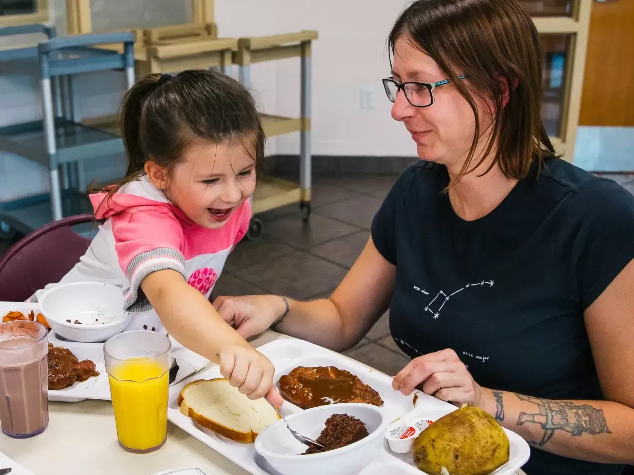 Woman and girl eating lunch. Girl is reaching across to grab a bite of cake.