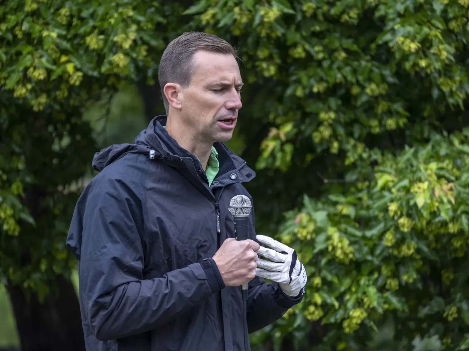 Man in a golf glove holding a microphone and praying