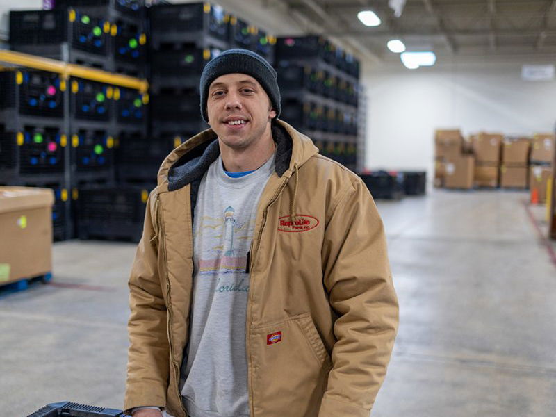 man in a tan coat and navy beanie standing in a warehouse