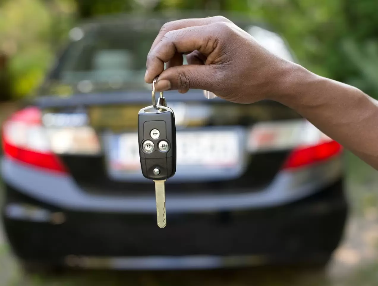 Close up of someone holding a car key with a black sedan in the background