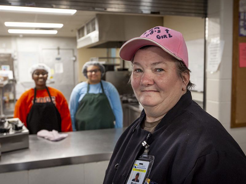 woman in a pink ballcap standing in front of a commercial kitchen serving area